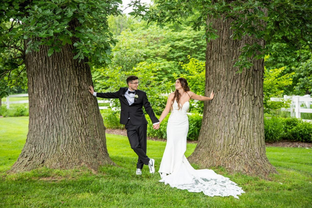 A man and woman in a suit and tuxedo holding hands and standing next to trees