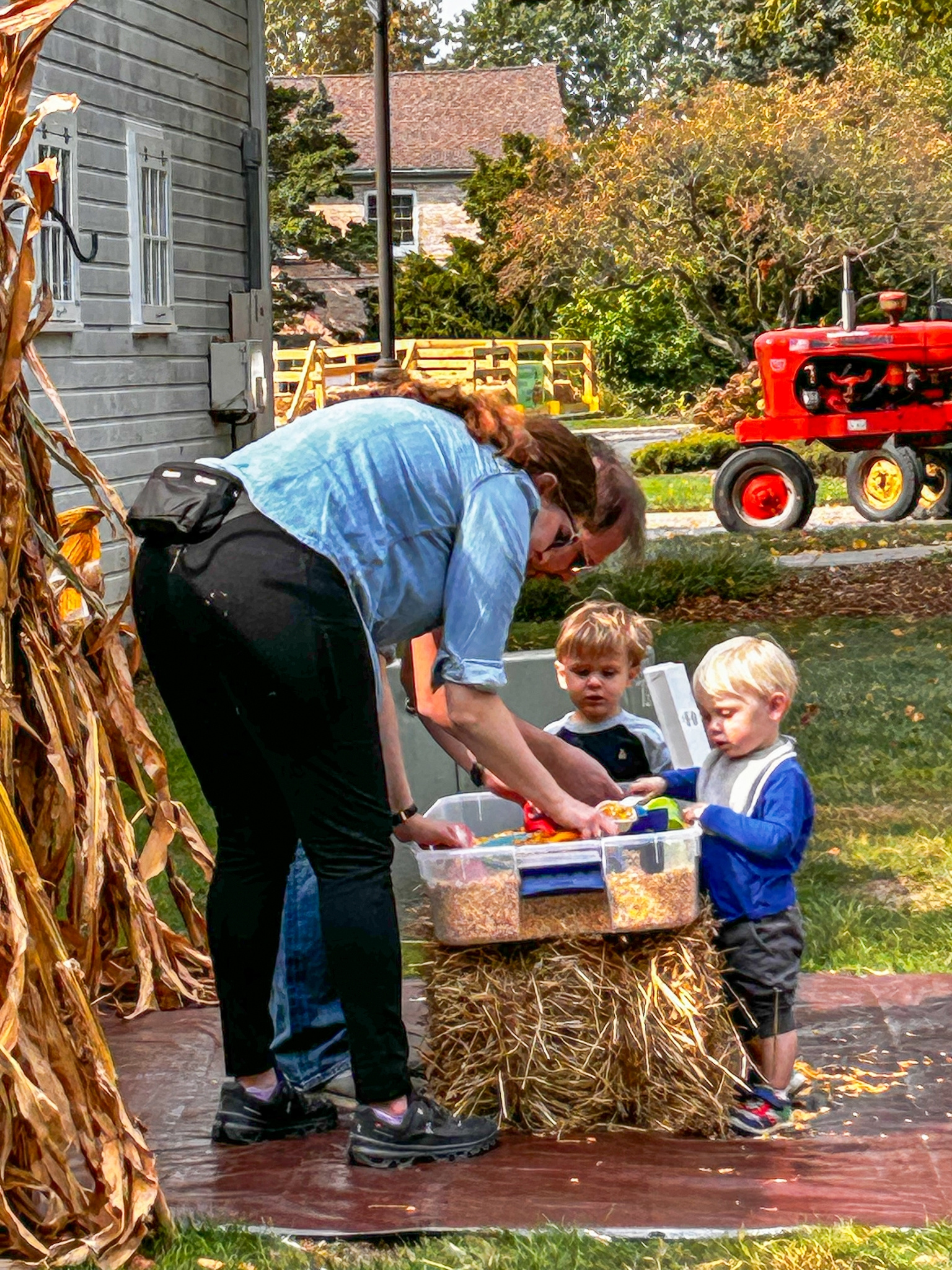 Young children enjoying a corn activity near a red tractor during a previous festival